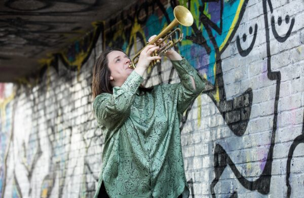 Charlotte Keeffe playing trumpet in grafitti walled underpass