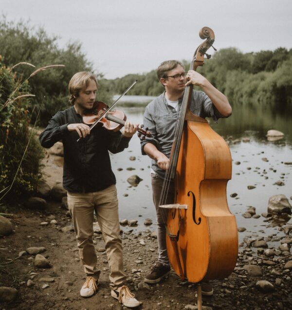 two people playing violin and double bass beside a stream