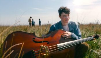 Young man sitting in a field with a double bass