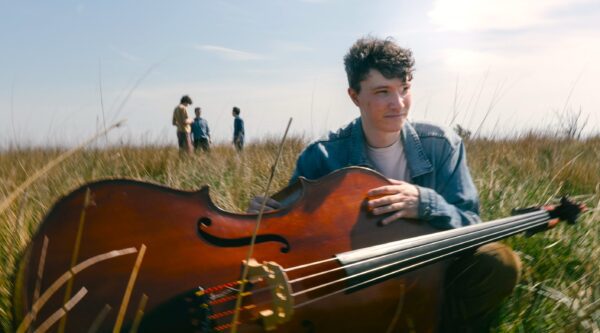 Young man sitting in a field with a double bass