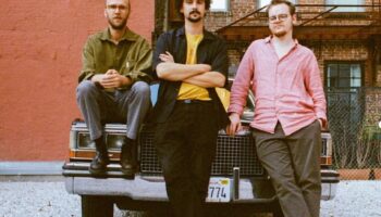 Three band members sitting on bonnet of vintage American car