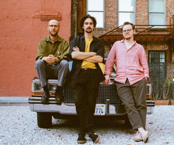 Three band members sitting on bonnet of vintage American car