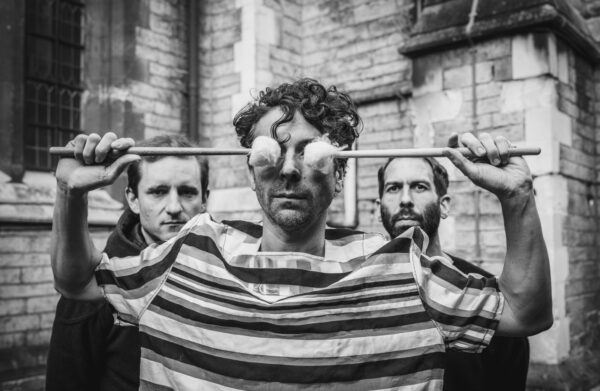 The trio pictured with drummer holding soft head sticks over his eyes