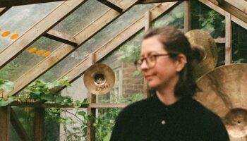 Sarah Heneghan in green house with hanging cymbals